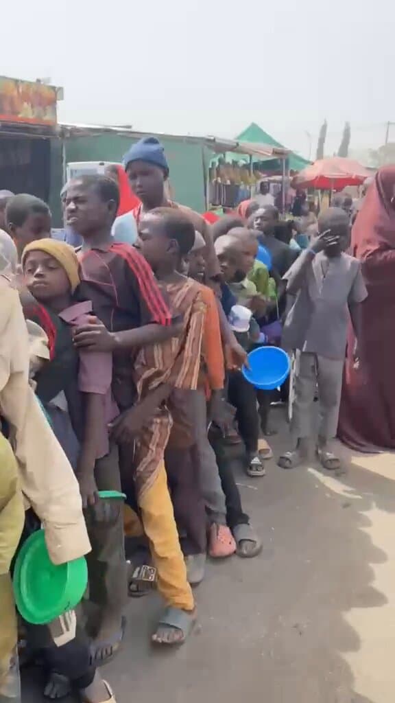 A long queue of children holding bowls at a daytime food distribution
