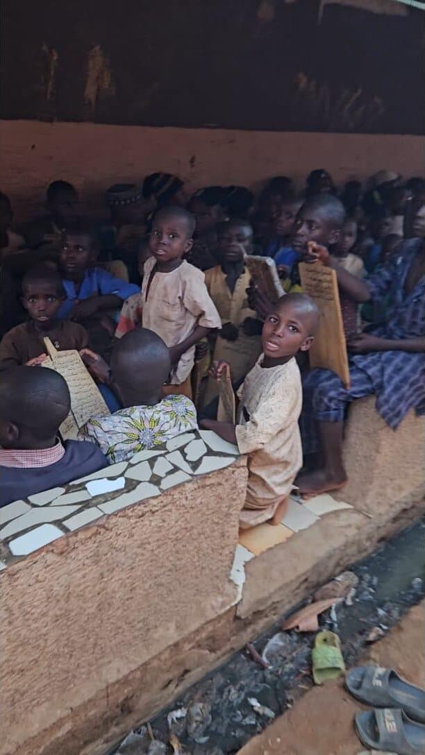 Children seated together with study tablets at an outdoor Quranic school