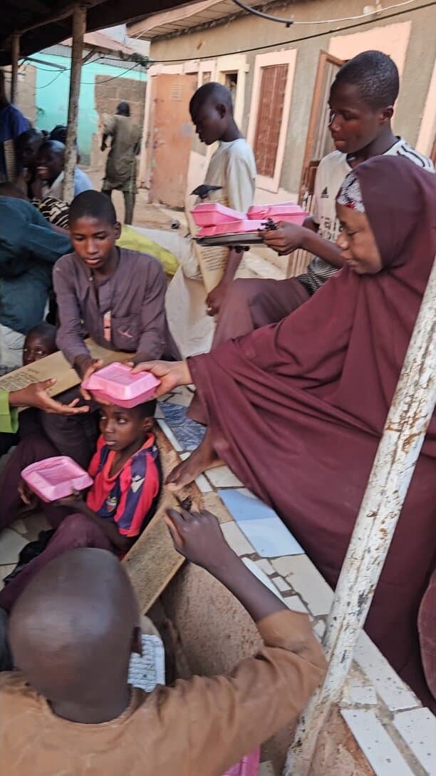 A volunteer hands a packed meal to a child during a Hajiya Nafisa Foundation food distribution in Kaduna