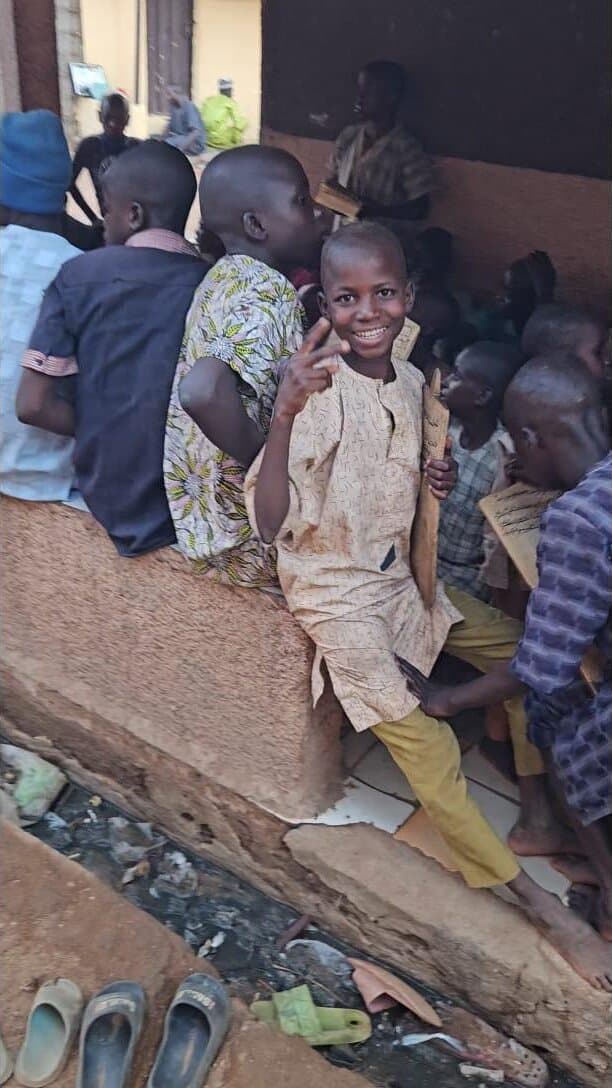 A smiling boy among classmates at an outdoor Quranic school in Kaduna